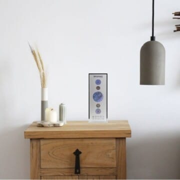 BioSpace 8V11 Diamond on a wooden table. The product features a sleek design with a display showing three circular elements, set against a simple background. A grey pendant light hangs above, complementing the modern decor.