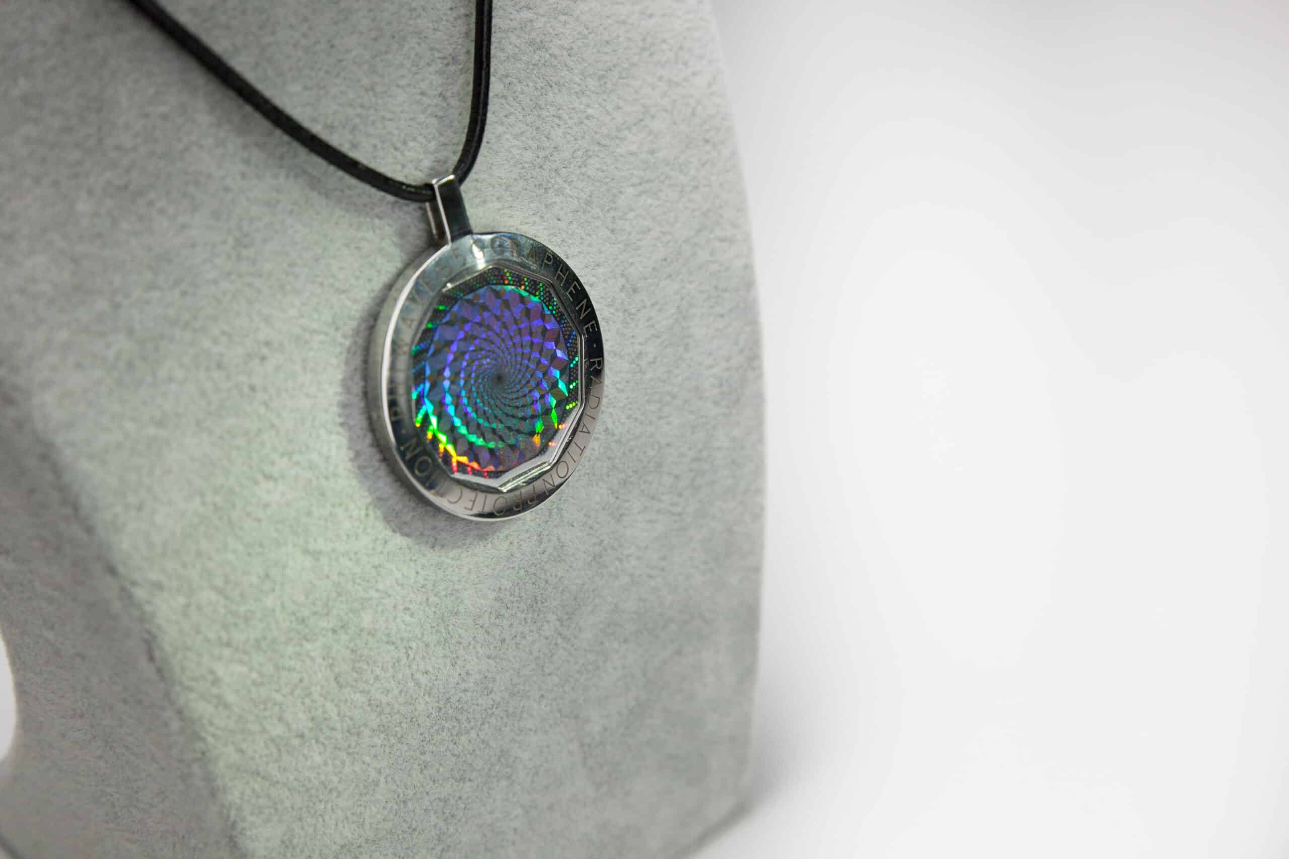 PhiWaves Jewel Diamond pendant featuring a holographic design in a circular shape, suspended on a black cord, showcasing an iridescent spiral pattern against a grey background.