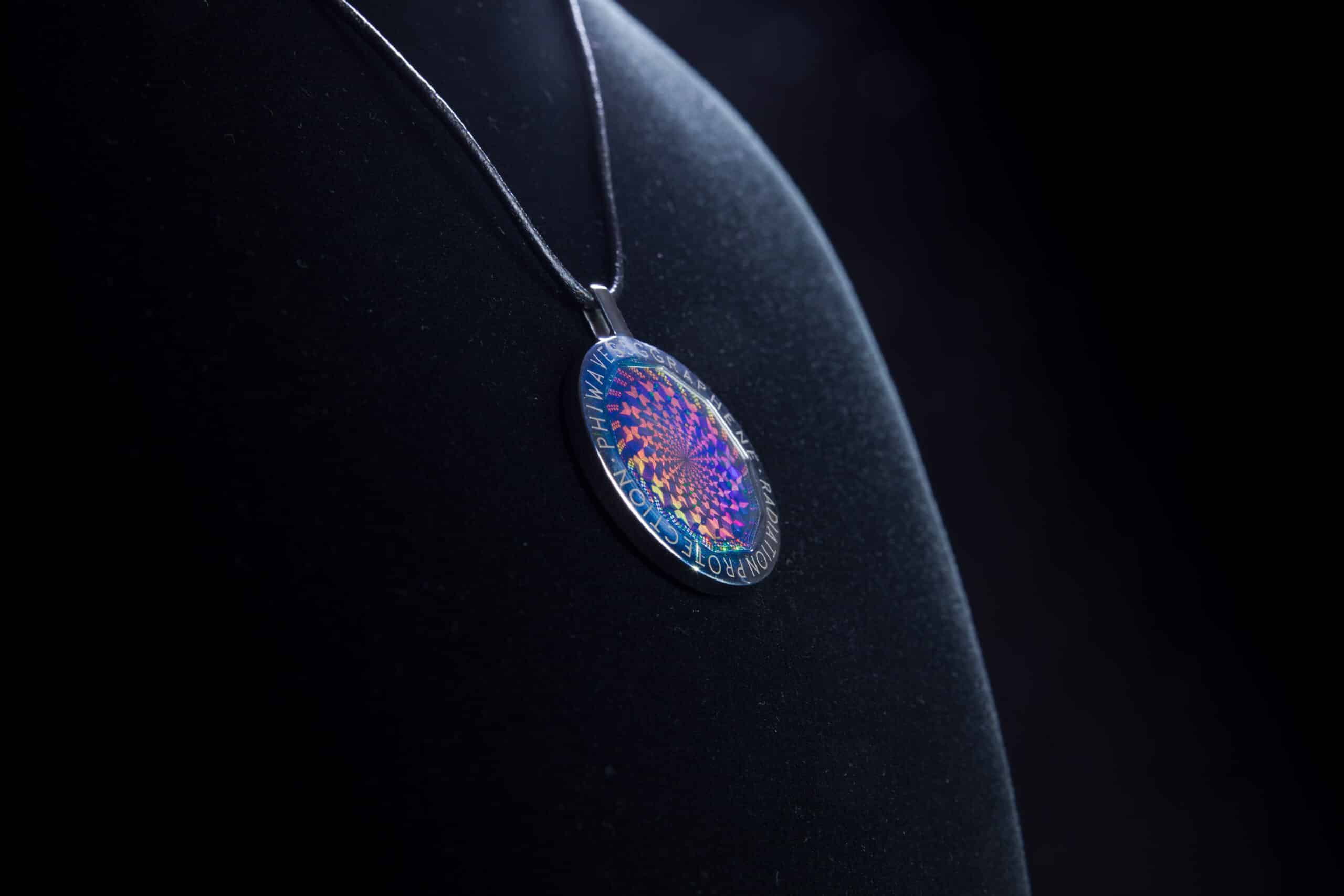 PhiWaves Jewel Diamond pendant displayed on a black surface, featuring a circular design with an intricate colorful pattern. The pendant is suspended from a black chain, emphasizing its vibrant and reflective surface.