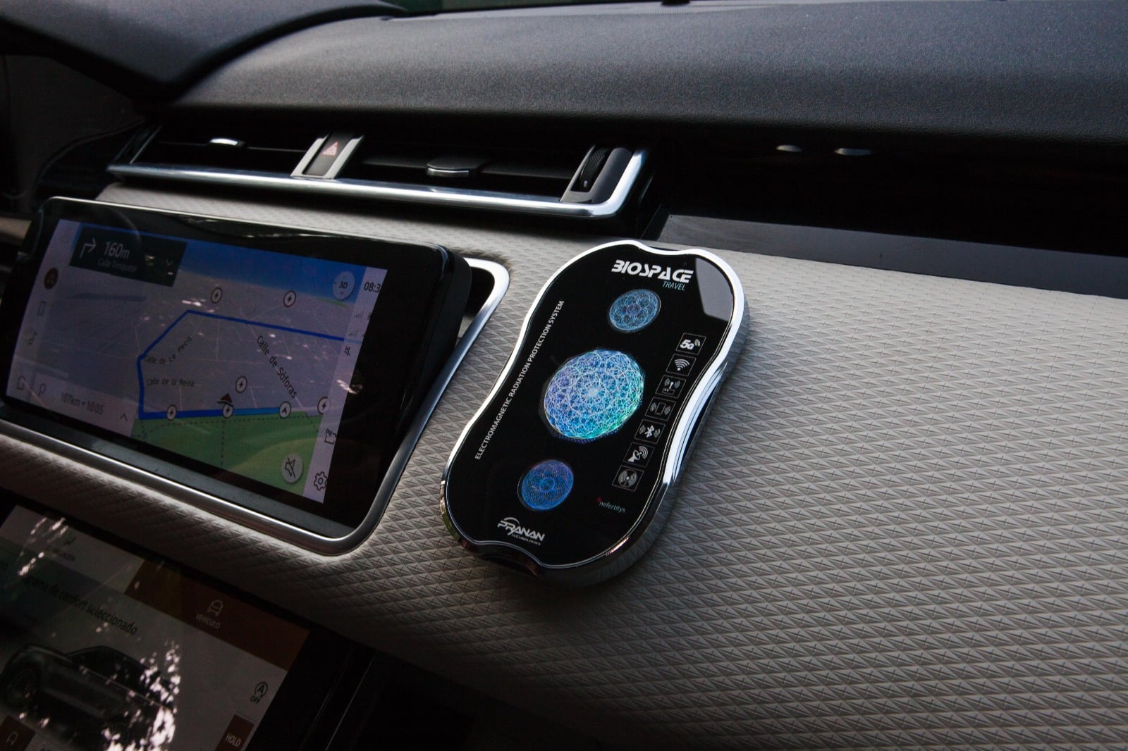 BioSpace Travel Diamond in black, featuring a sleek design with a digital display and control buttons. It is shown mounted on a car dashboard next to a smartphone displaying a navigation app.